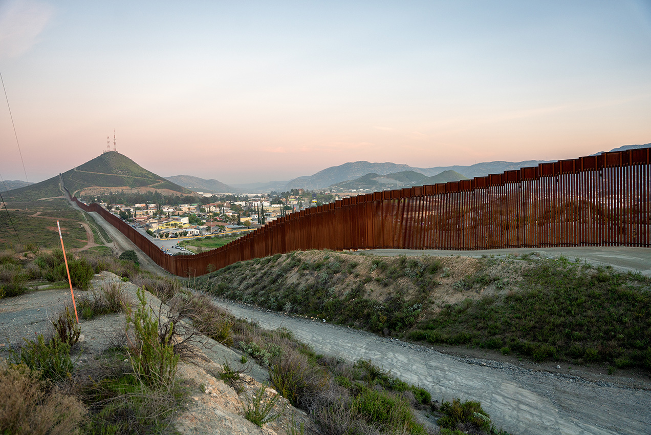 In an aerial view, a U.S. Border Patrol agent stands while looking through the U.S.-Mexico border fence.