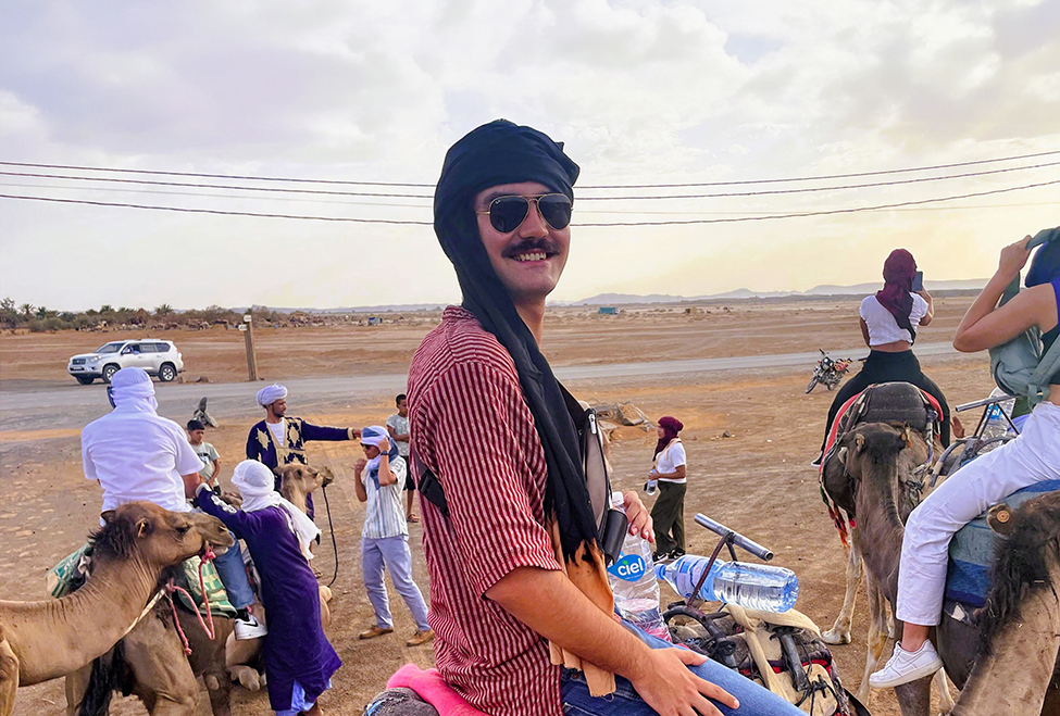 young man with mustache and sunglasses sitting on a camel in Morocco