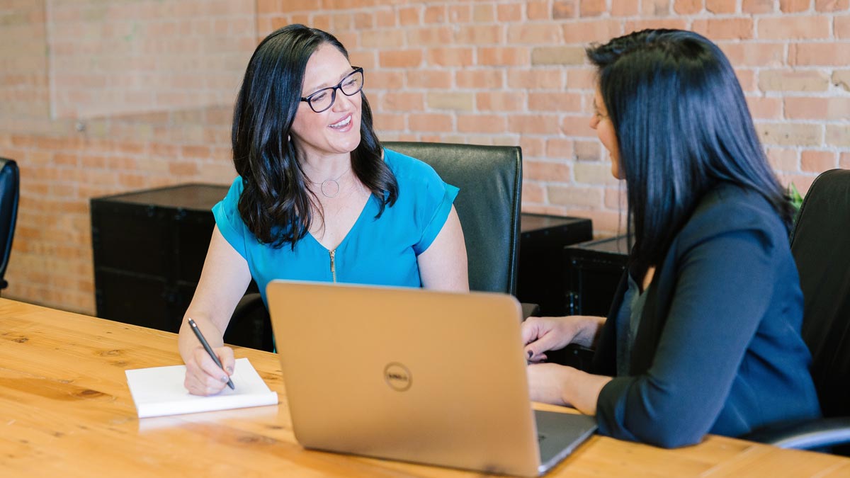 Two people talking at a table in front of a laptop