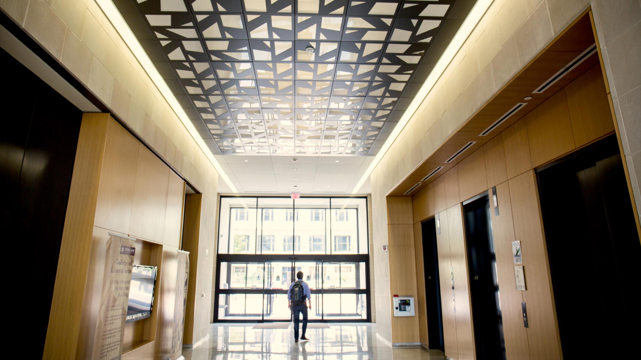 Student with a backpack walking towards glass exit doors