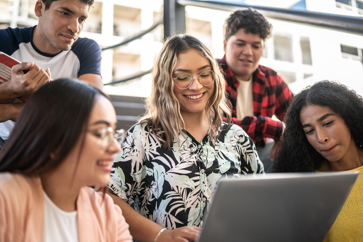 smiling students looking at the work on one studen'ts computer