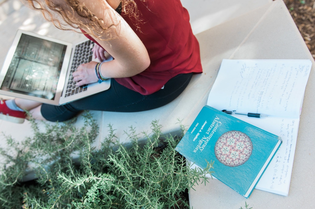 A girl sits on her laptop computer with a book behind her that reads "Contemporary Abstract Algebra".