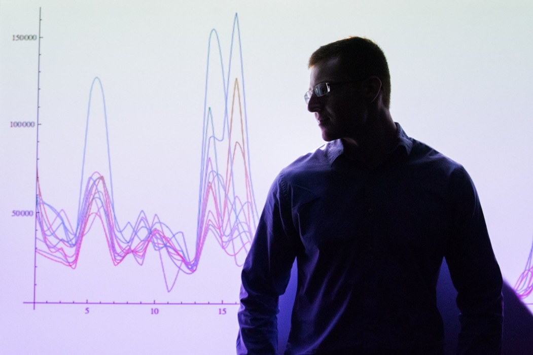 A dark silhouette of a man is in view as he stands in front of a large graph projected on the wall.