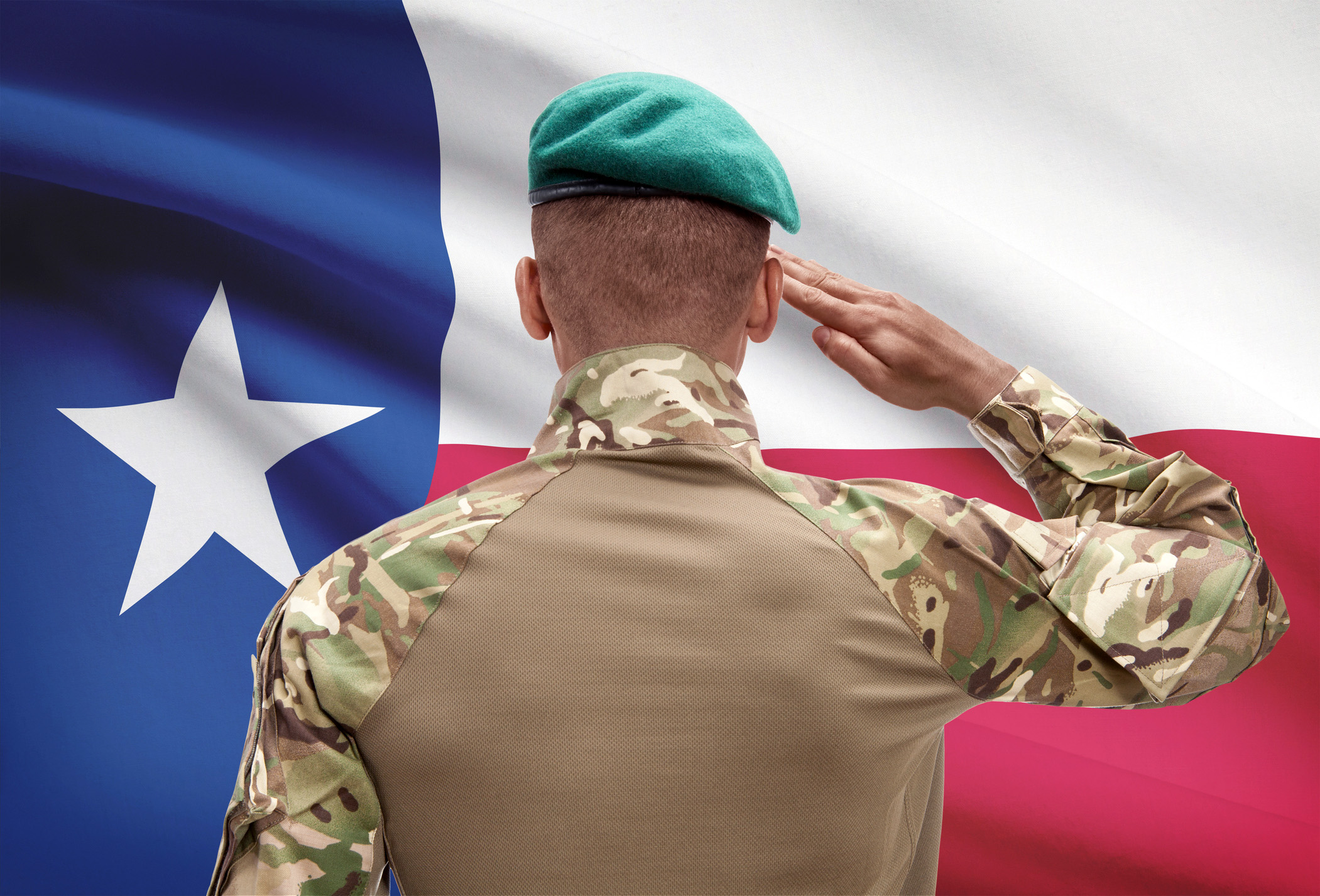 Male soldier dressed in camouflage fatigues and a green beret with his back to the viewer, saluting the State of Texas flag