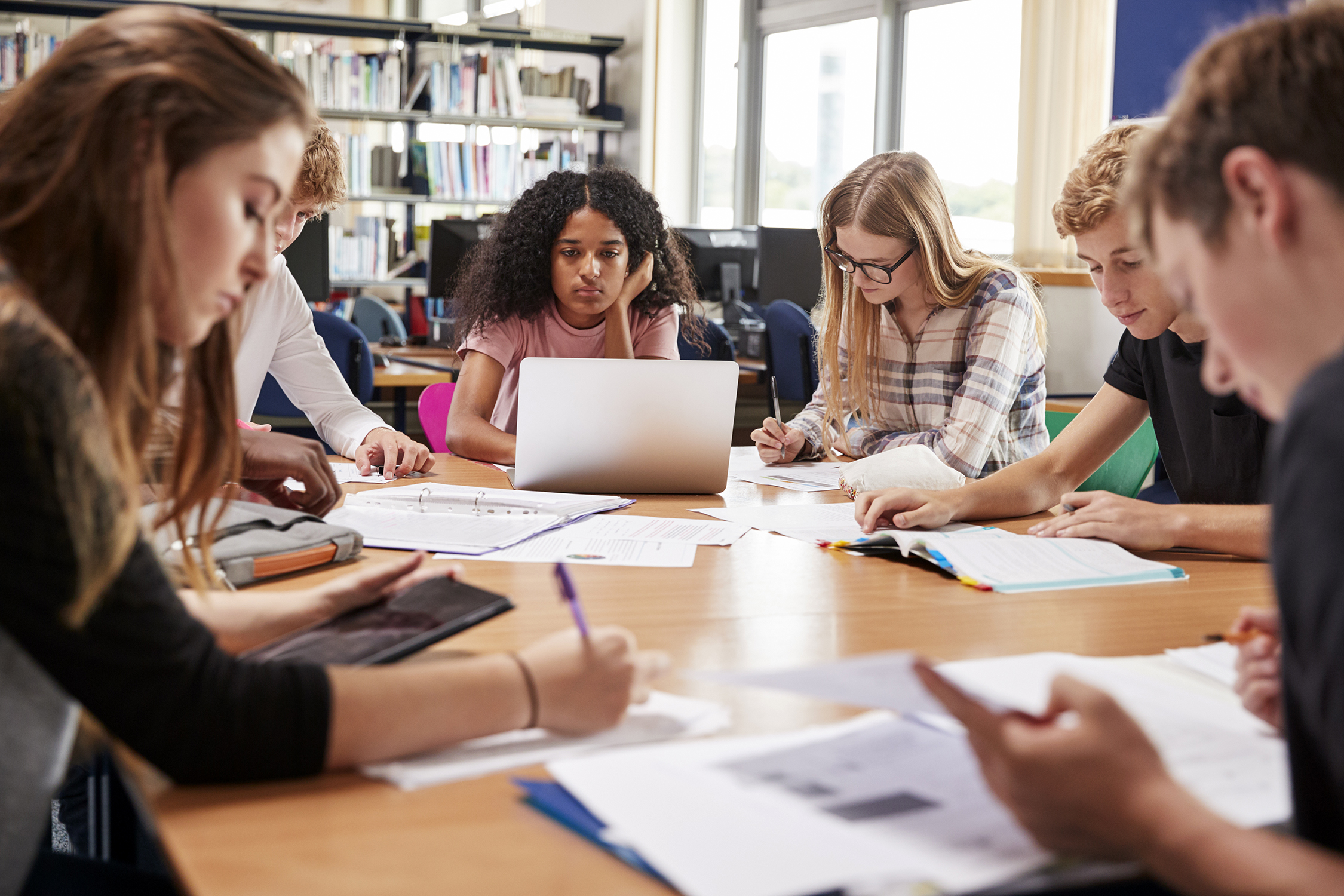 A group of male and female students working around a table within a library