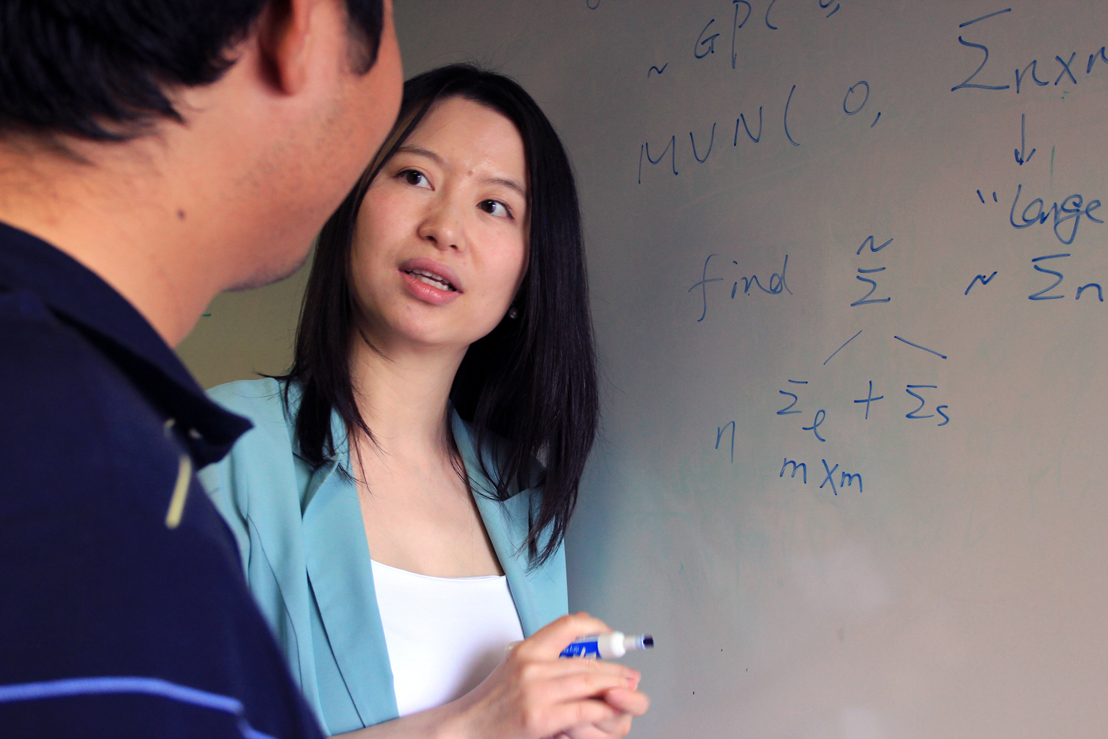 Texas A&M University statistician Huiyan Sang writes formulas on a dry erase board and explains them to a student