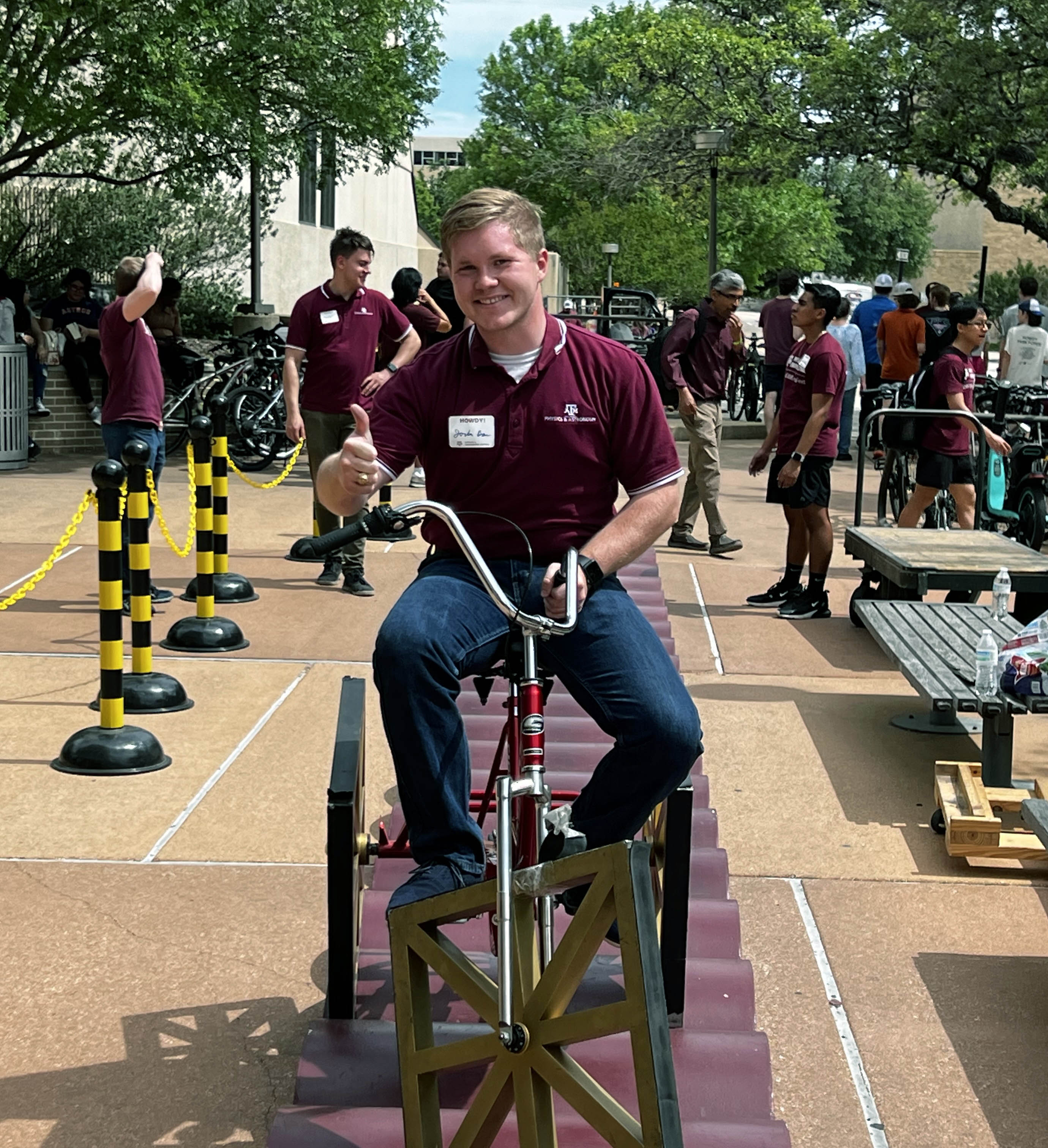 2024 Texas A&amp;M University physics graduate Jordan Bass flashes a gig 'em while riding the square-wheeled bicycle during the 2024 Physics and Engineering Festival on the Texas A&amp;M campus