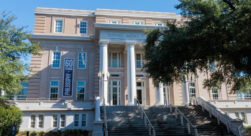 Exterior view of the Young Men’s Christian Association building on the campus of Texas A&M with a banner celebrating 60 years of philosophy on the left side of the building.