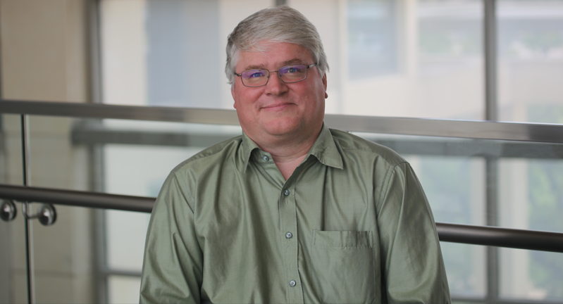 Dr. James Smith in an olive button down smiling in front of a sunny window