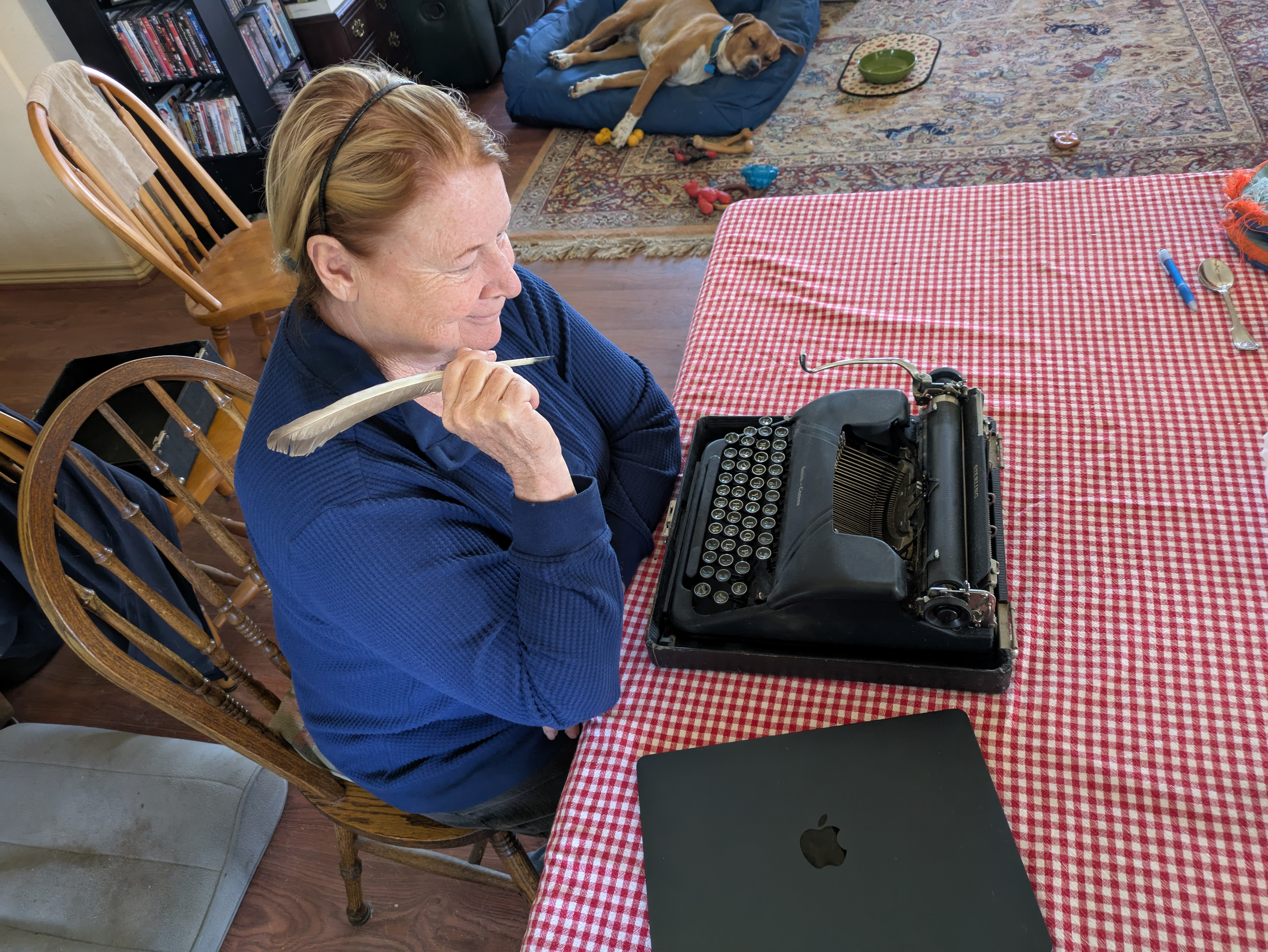 Margaret Ezell sits at a table holding a quill pen. On the table sits a typewriter and a laptop.