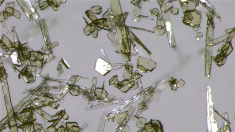 Microscopic view of crystalline structures, featuring various irregular shapes and sizes, on a light background that was synthesized in the Altman lab.