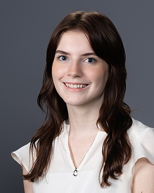 Headshot of Casey Delaney '29, wearing a white blouse against a grey background.