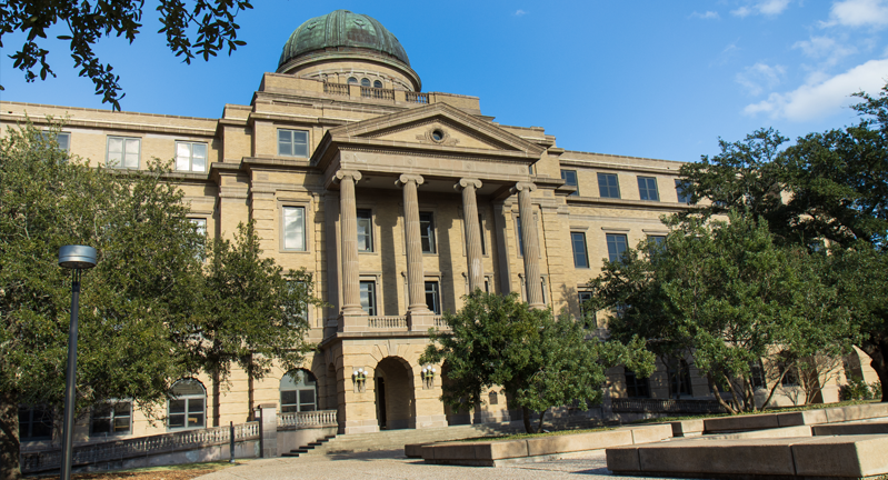 Exterior view of the Texas A&M University Academic Building on a sunny day, showing its classic architecture with a large dome and multiple columns.