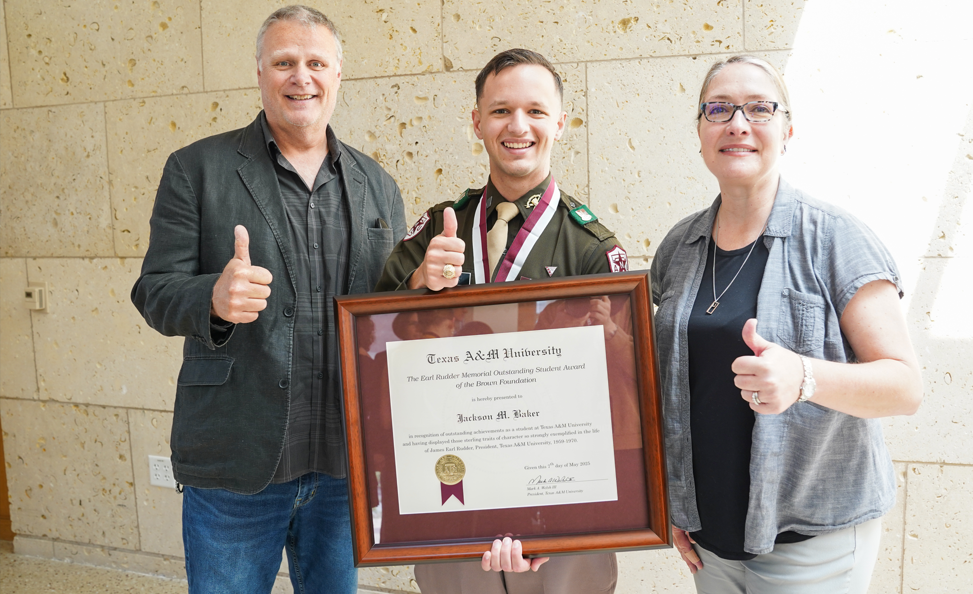 Dr. Darryl De Ruiter, Jackson Baker, and  Dr. Angela P. Hudson pose for a photo, with Baker holding a framed award certificate. All three are giving a thumbs-up.