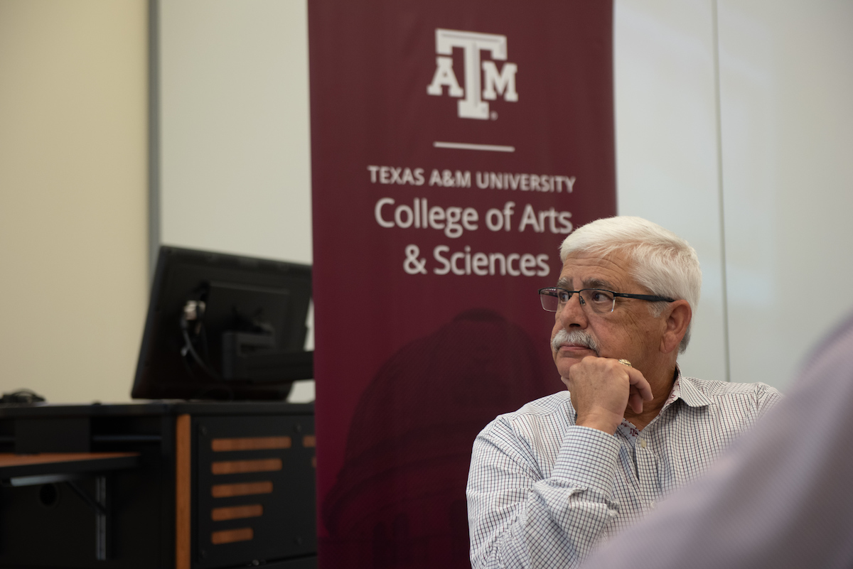 man seated in front of the College of Arts and Sciences banner