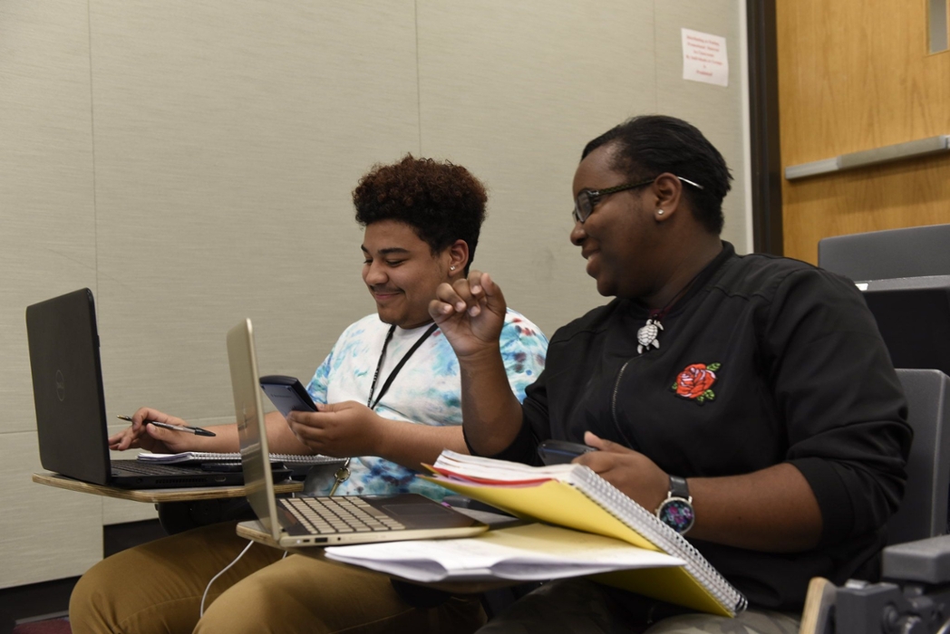 Two happy students working next to each other on a statistics project.