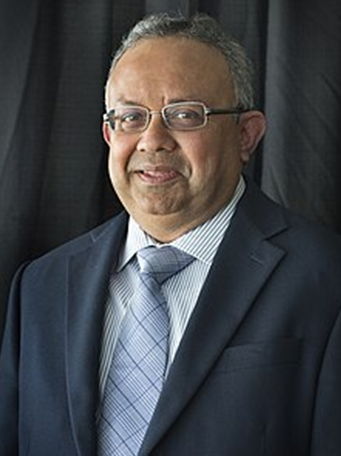 Portrait of Dr. Dipak Deyin a dark suit and plaid tie, smiling at the camera.